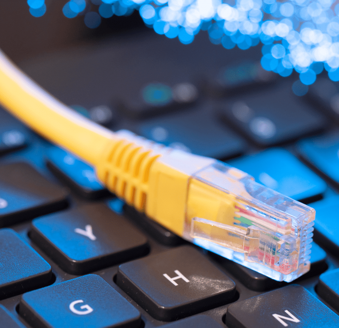 A yellow Ethernet cable rests on a black computer keyboard, with blue lights and blurred fiber optic strands in the background, symbolizing internet connectivity and technology.