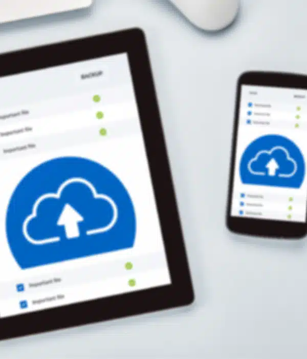 A tablet and a smartphone display cloud backup icons and file lists on their screens, suggesting cloud storage or data synchronization. The devices are on a light-colored surface.